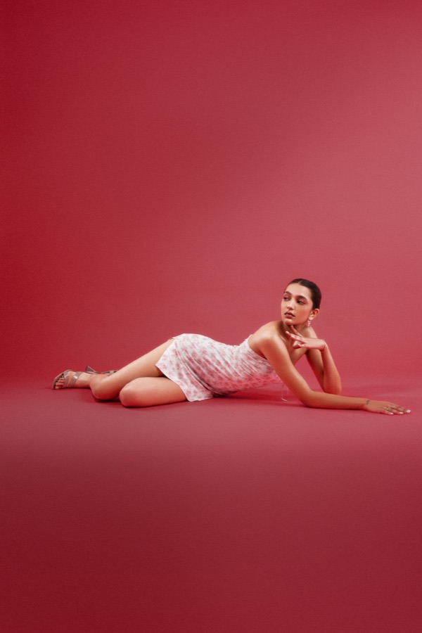 Commercial campaign — reclining in a floral mini dress against a crimson backdrop