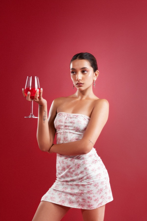 Commercial campaign — holding a glass of wine in a floral dress on crimson backdrop