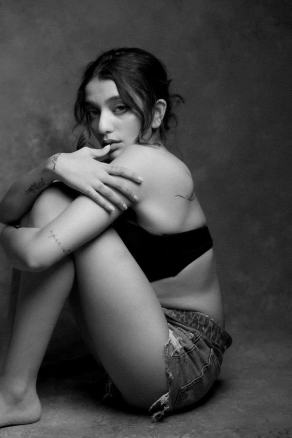 Black and white portrait — seated hugging her knees, soft gaze
