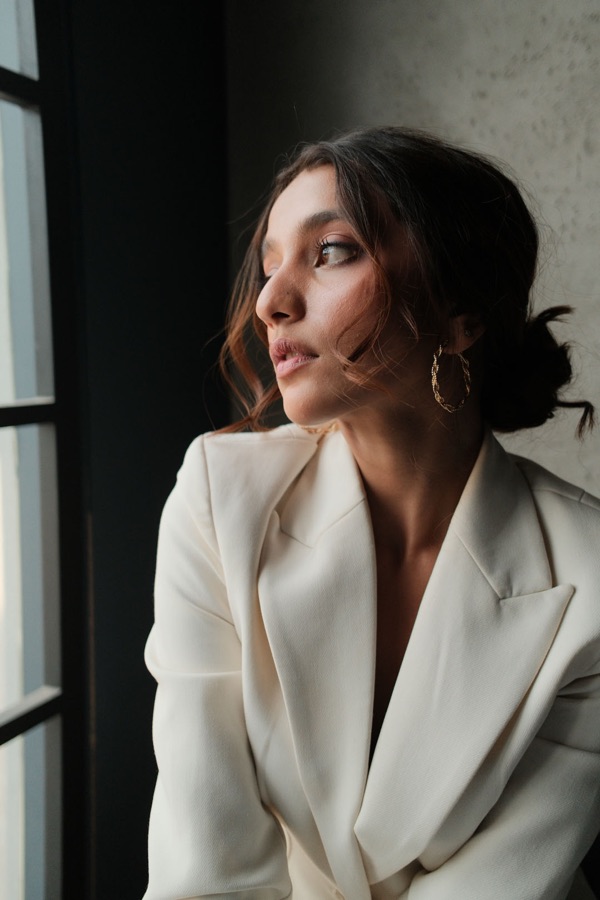 Portrait by window light in a cream blazer, gazing outward