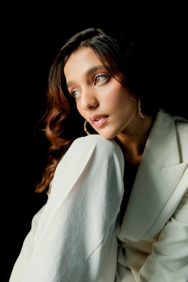 Portrait in a white blazer against a black background, looking over her shoulder