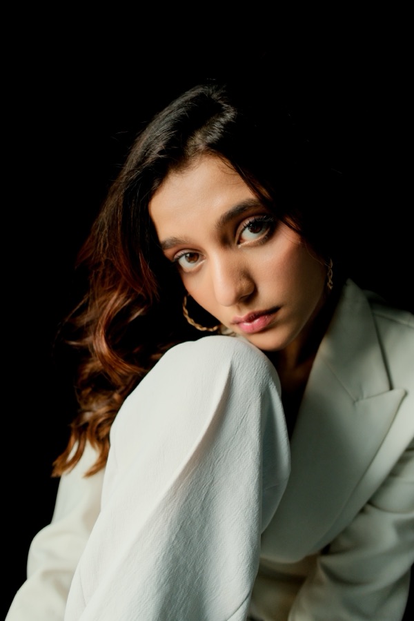 Portrait in a white blazer, direct steady gaze against black