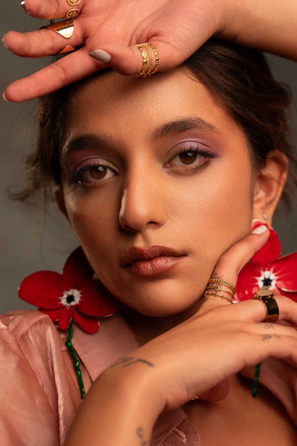 Beauty close-up with red flower earrings, gold rings and lilac eyeshadow