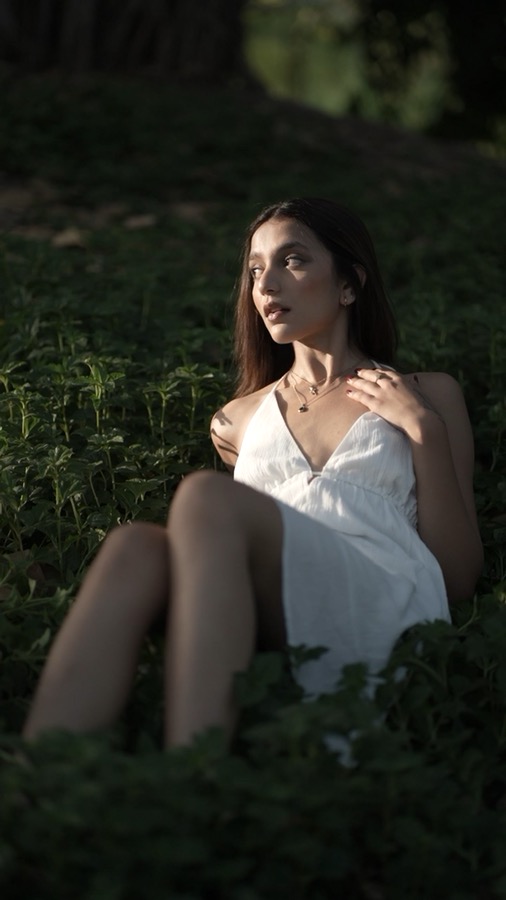 Video still — reclining in greenery in a white dress at golden hour