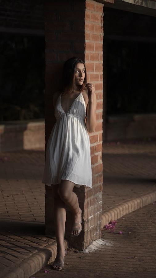 Video still — full-length look in a white mini dress beside a brick pillar