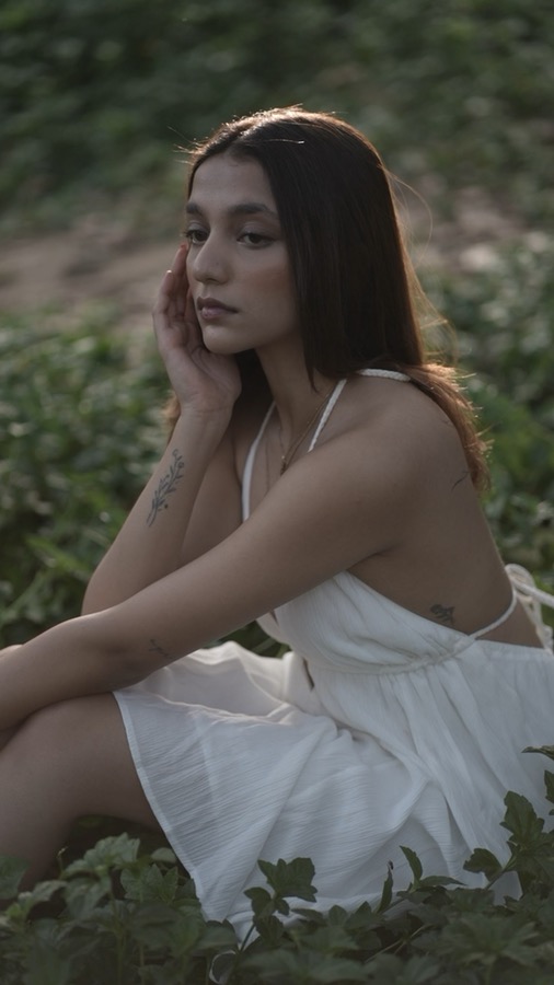 Video still — seated among wild greenery in a white dress