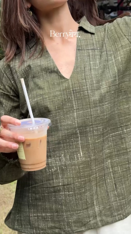 Video still — lifestyle UGC clip holding an iced coffee in an olive shirt